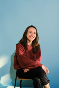 Larissa Lachmann in rotem Pulli lachend auf einem Stuhl.